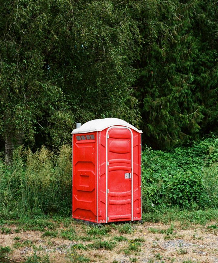 Toilette de chantier autonome rouge installée en bordure d'un terrain arboré